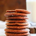 A tall stack of ginger snap cookies with a glass of milk in the background