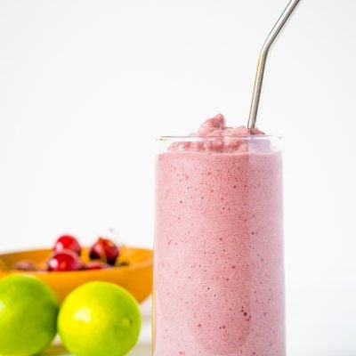 A smoothie made with cherries in a tall glass with a metal straw on a white background