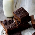 A stack of gluten-free brownies on a wood table with some milk