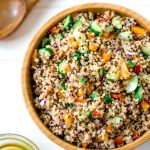Overhead shot of a big wooden bowl of zesty quinoa salad on a white background with some dressing on the side.
