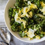 A bowl of roasted kale and napa cabbage on a grey wood table with serving spoons