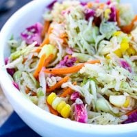 Homemeade coleslaw made with an oil and vinegar base held in a crisp white bowl over a royal blue napkin