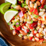 Mexican bean salad on a large wooden bowl with lime wedges