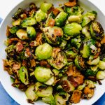 Pan seared brussel sprouts and bacon in a white bowl over a blue napkin