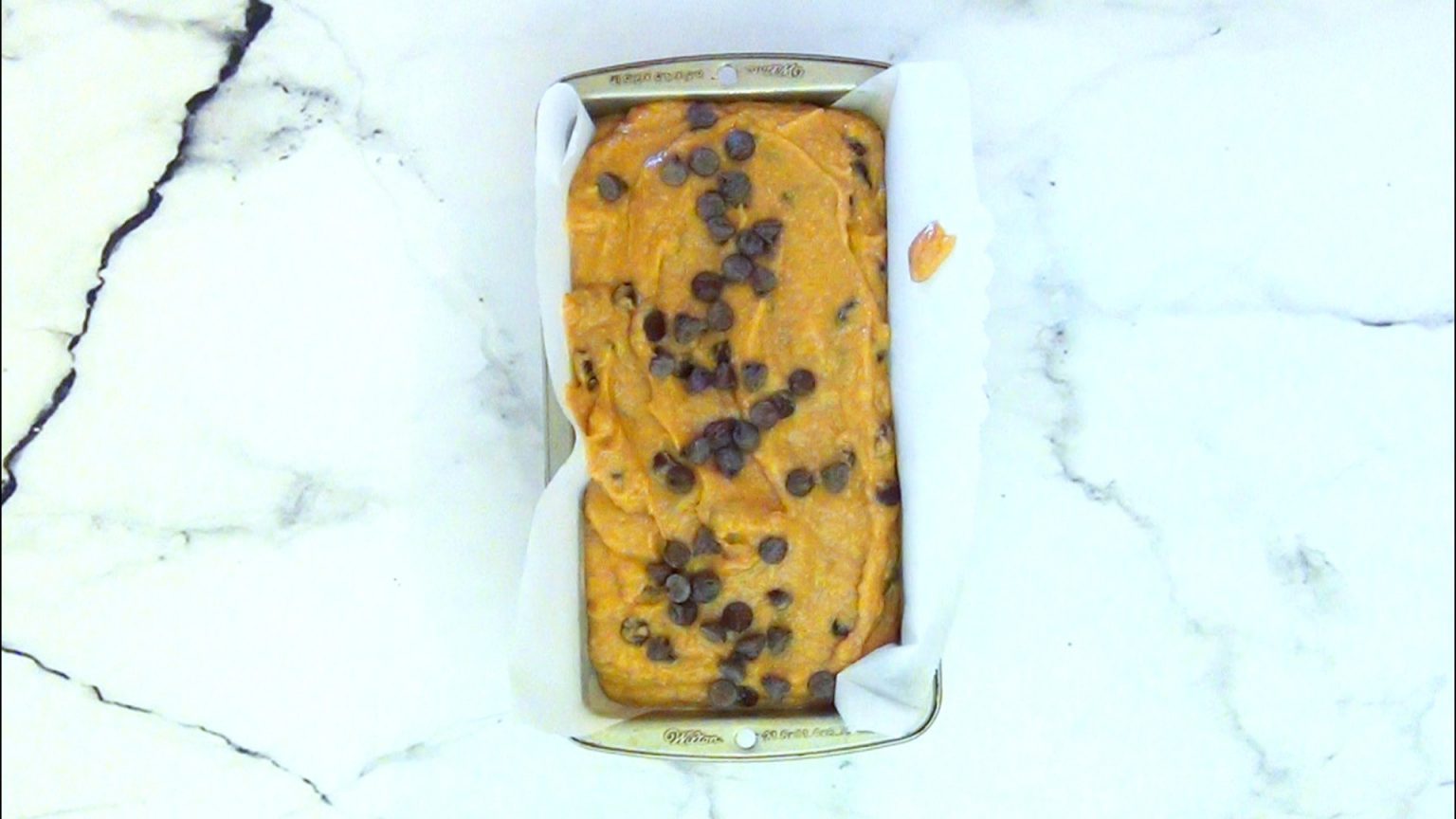 A loaf pan filled with chocolate chip pumpkin bread batter with more chips on top