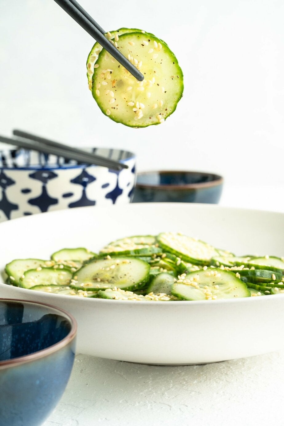 chop sticks picking out a few slices of cucumber out of a bowl of cucumber salad