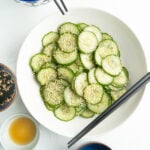 A Sesame Cucumber Salad Recipe on a white table with chopsticks blue serving bowls.