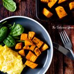 Overhead shot of a baking sheet of baked sweet potatoes and a plate of eggs