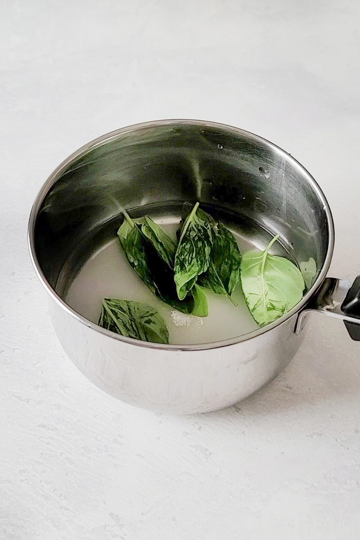 A pot of simple syrup and basil leaves.
