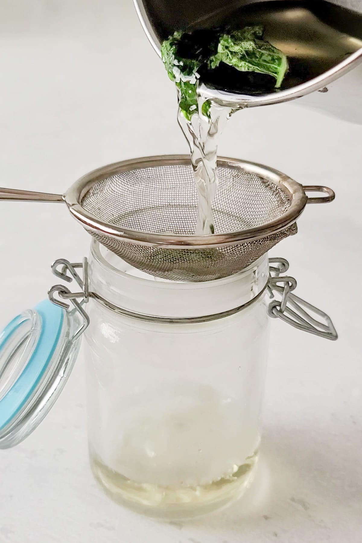 Basil simple syrup being poured into a jar using a small sieve.