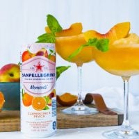 Two Bellini Mocktails in tall stemmed glasses topped with a peach wedge and basil #shop #cbias