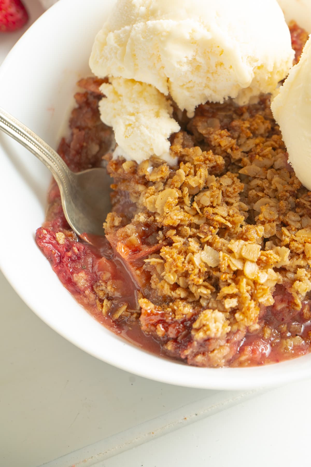 Gluten-free strawberry rhubarb crisp in a bowl with vanilla ice cream and a spoon.
