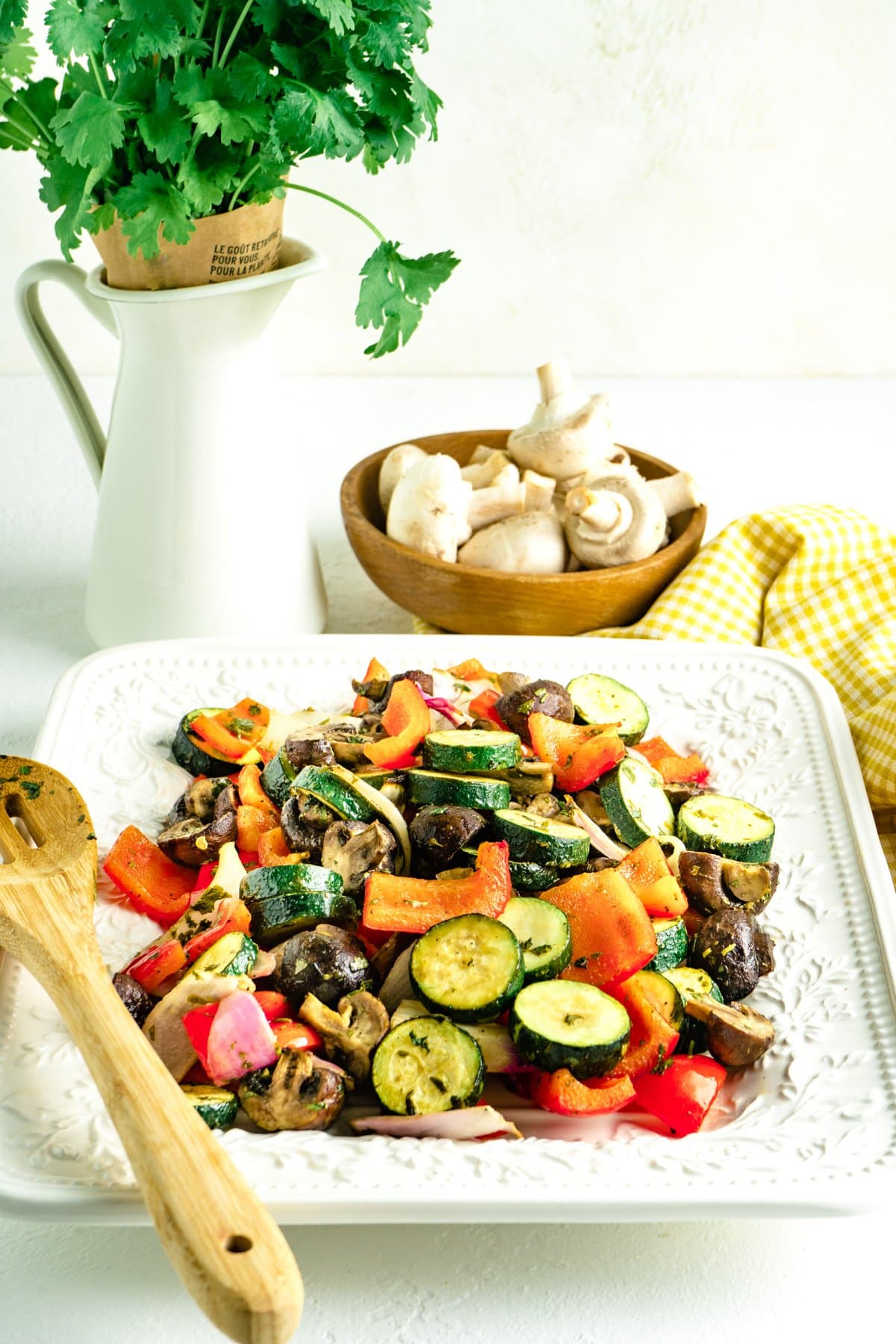 Mediterranean roasted vegetables on a white platter with a spoon and a bowl of mushrooms.