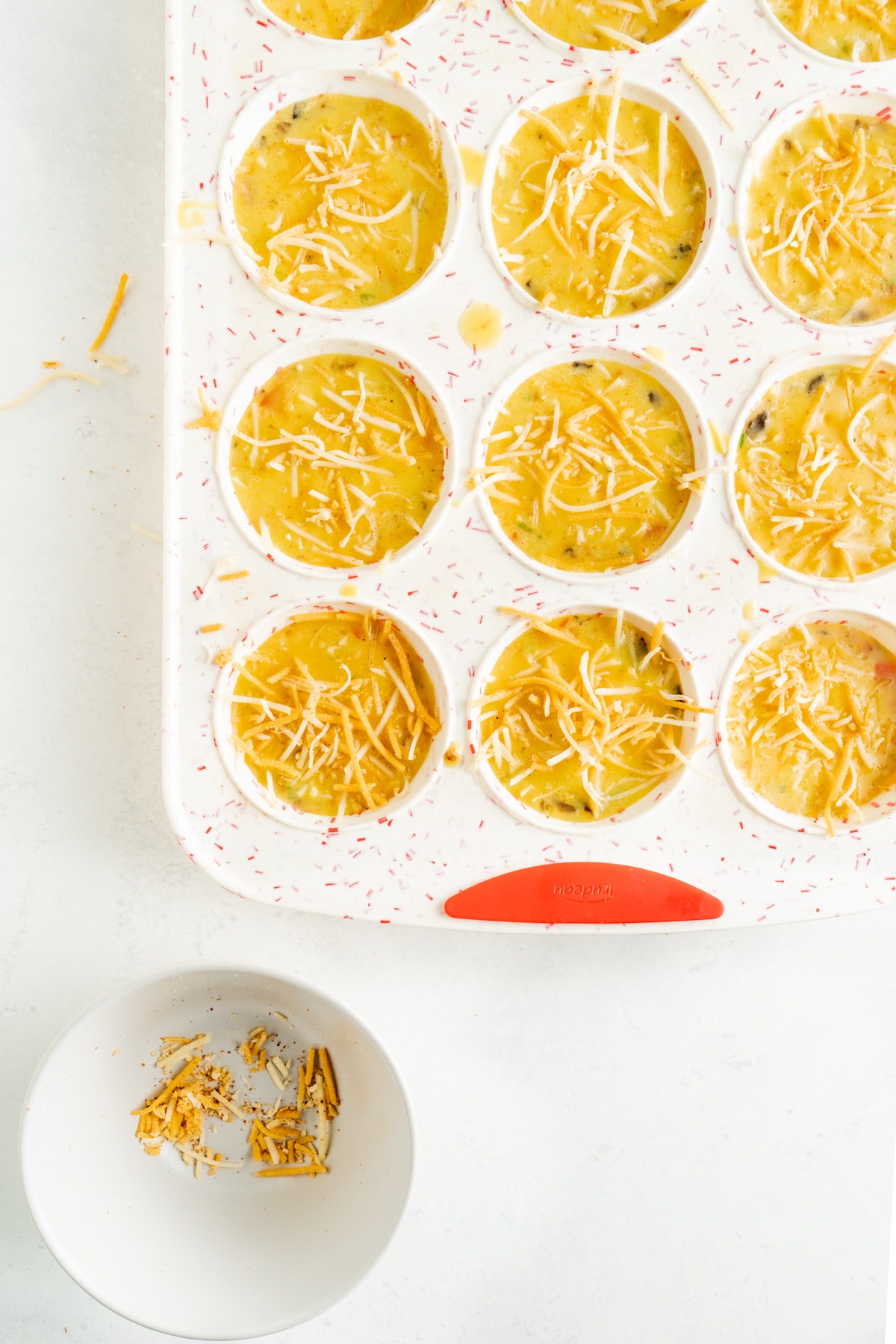 Omelet Bites raw in a muffin tin with cheese on top.