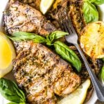 On overhead shot of a white platter of grilled pork chops decorated with grilled lemons and fresh basil leaves