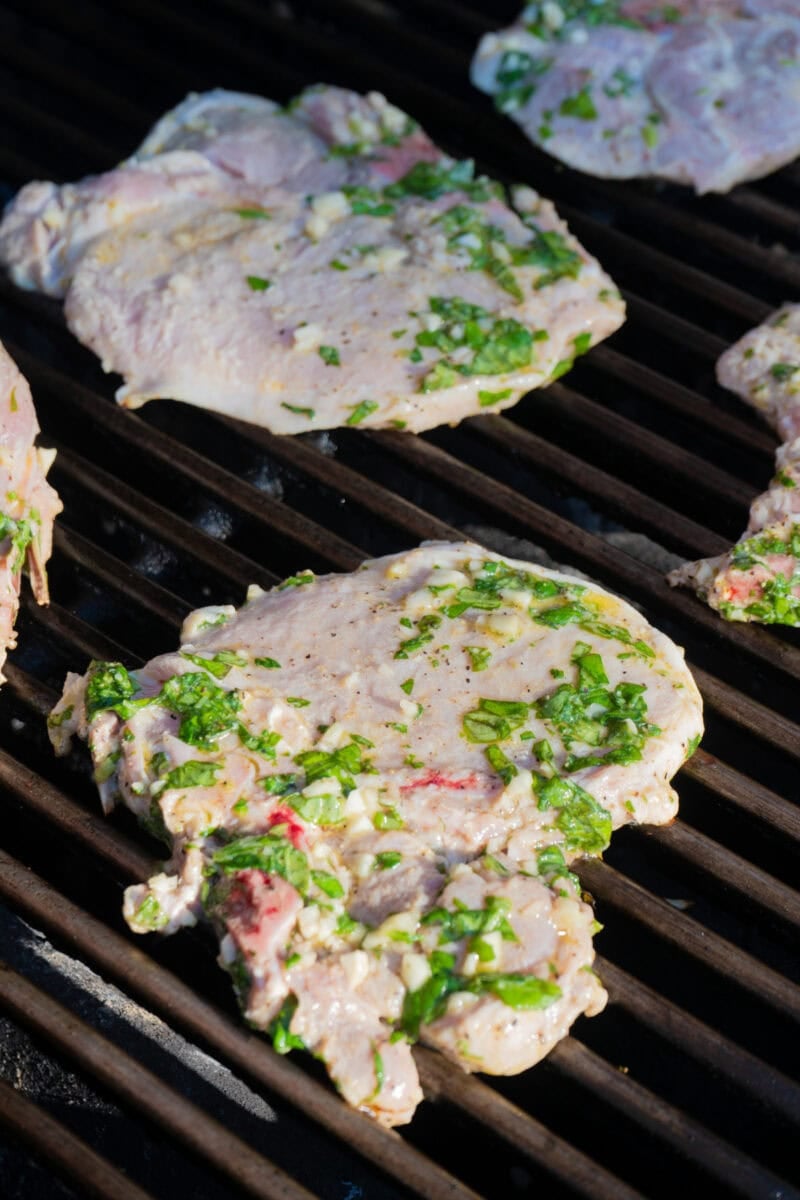 Pork chops covered in a basil marinade on the grill.