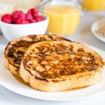 Close up of two pieces of french toast with some raspberries and a glass of orange juice in the background