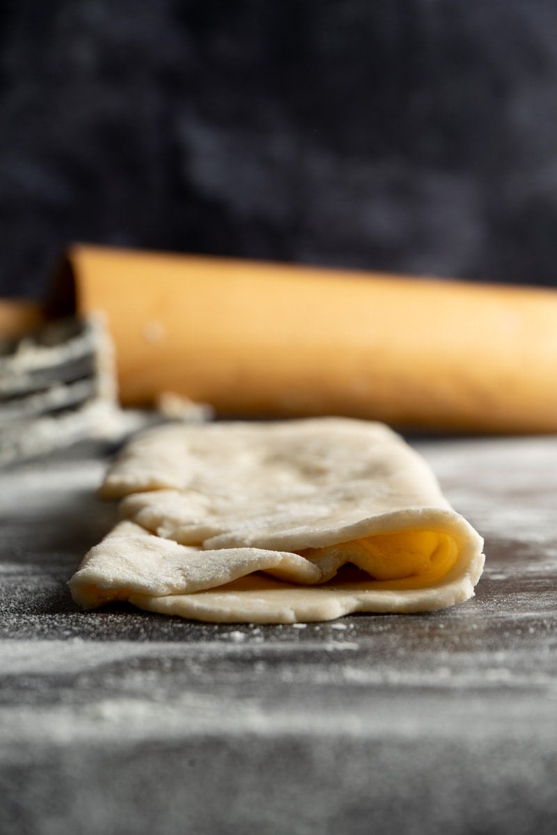 Dairy free pie crust rolled and folded over on a table with a rolling pin.