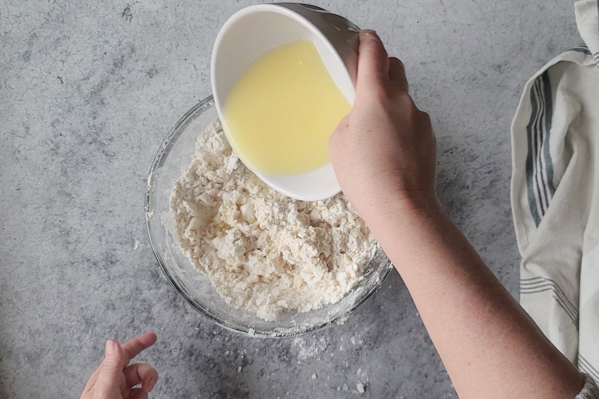 An egg mixture being poured into a bowl of flour and lard for a pie crust recipe.