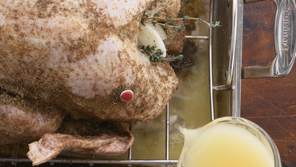 A pan for a convection roasted turkey with broth being added to the pan.