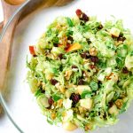 Brussel sprout salad in a glass bowl with some wooden spoons
