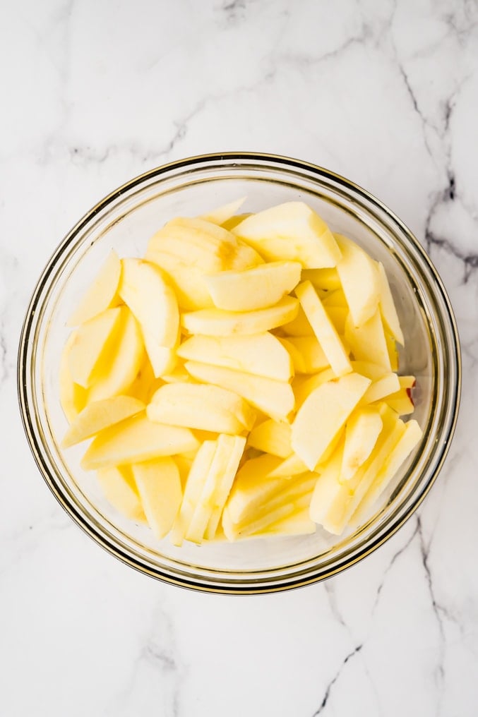 Overhead shot of a bowl of sliced apples on a white background