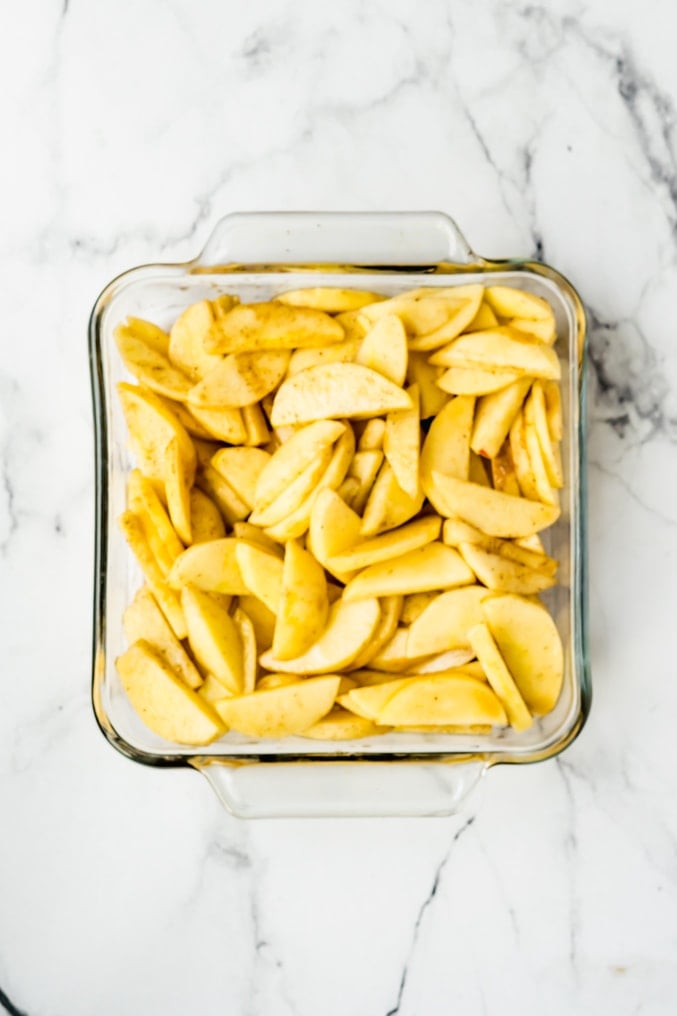 An 8 X 8 inch glass baking dish filled with seasoned apples on a white background
