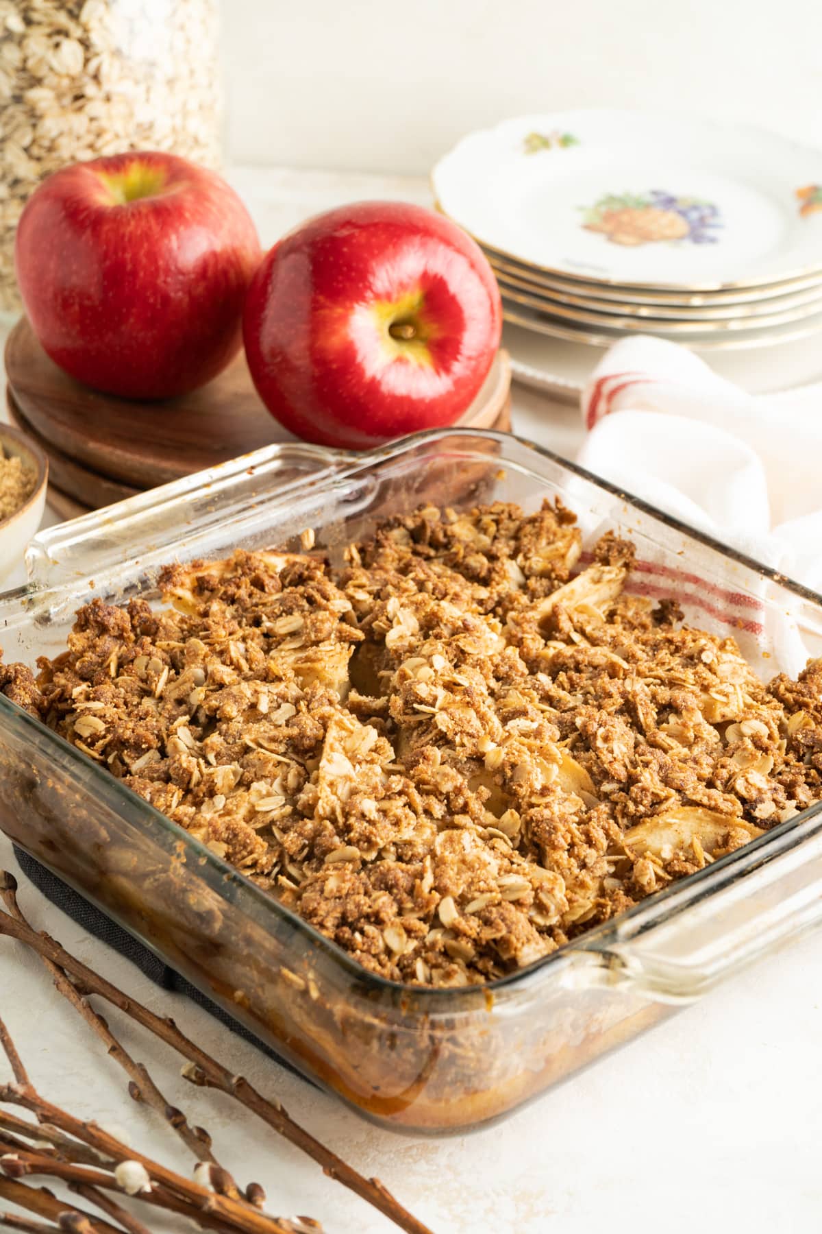 A baking dish frilled with apple crisp with plates and apples nearby.