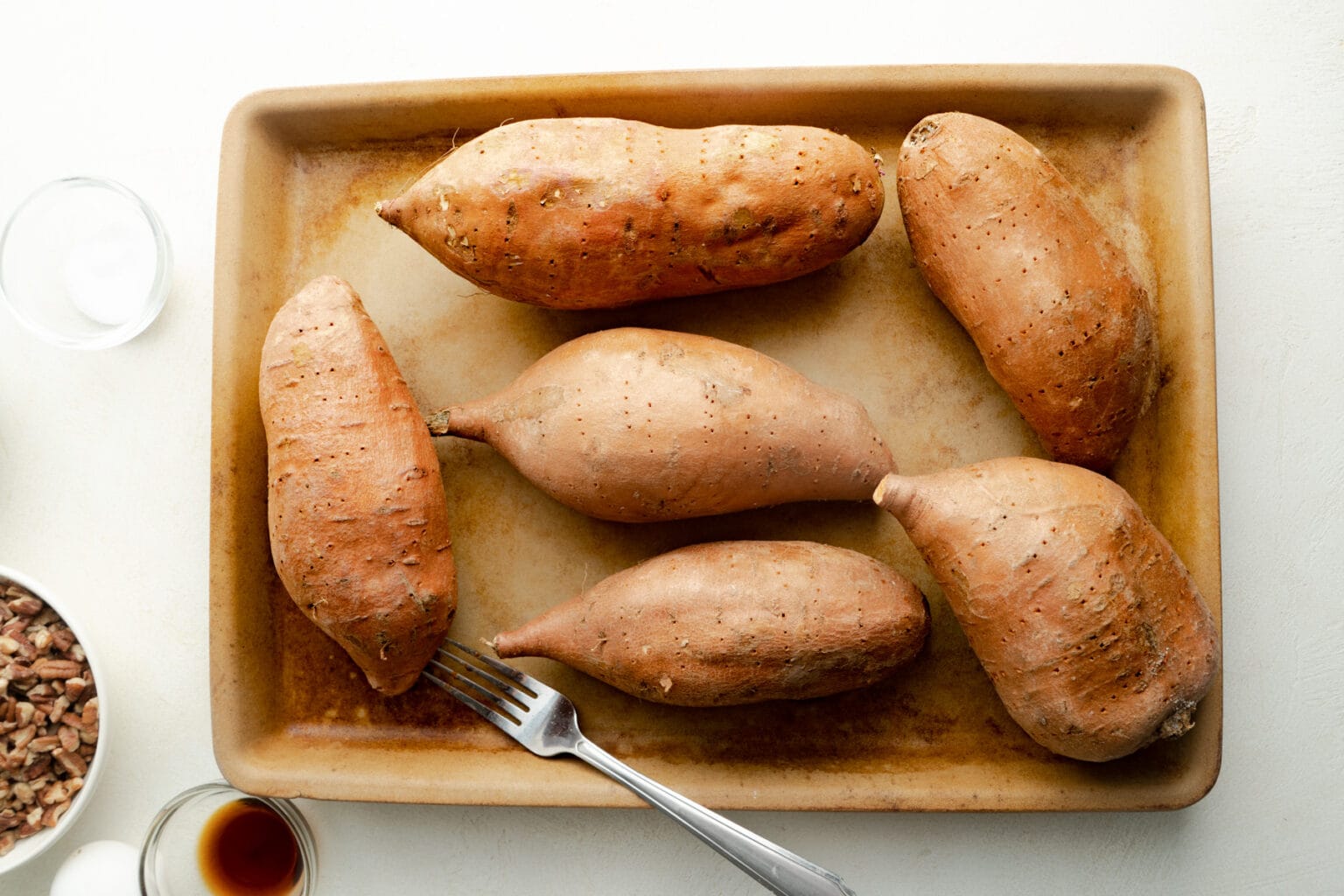 sweet potatoes punctured with a fork on a baking sheet.