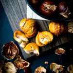 Shelled roasted chestnuts on a wood cutting board with shells all around
