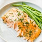 A large piece of baked salmon with dill and green beans on a grey plate.