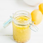 Lemon vinaigrette in a small mason jar on a whit table with a bowl of lemons nearby