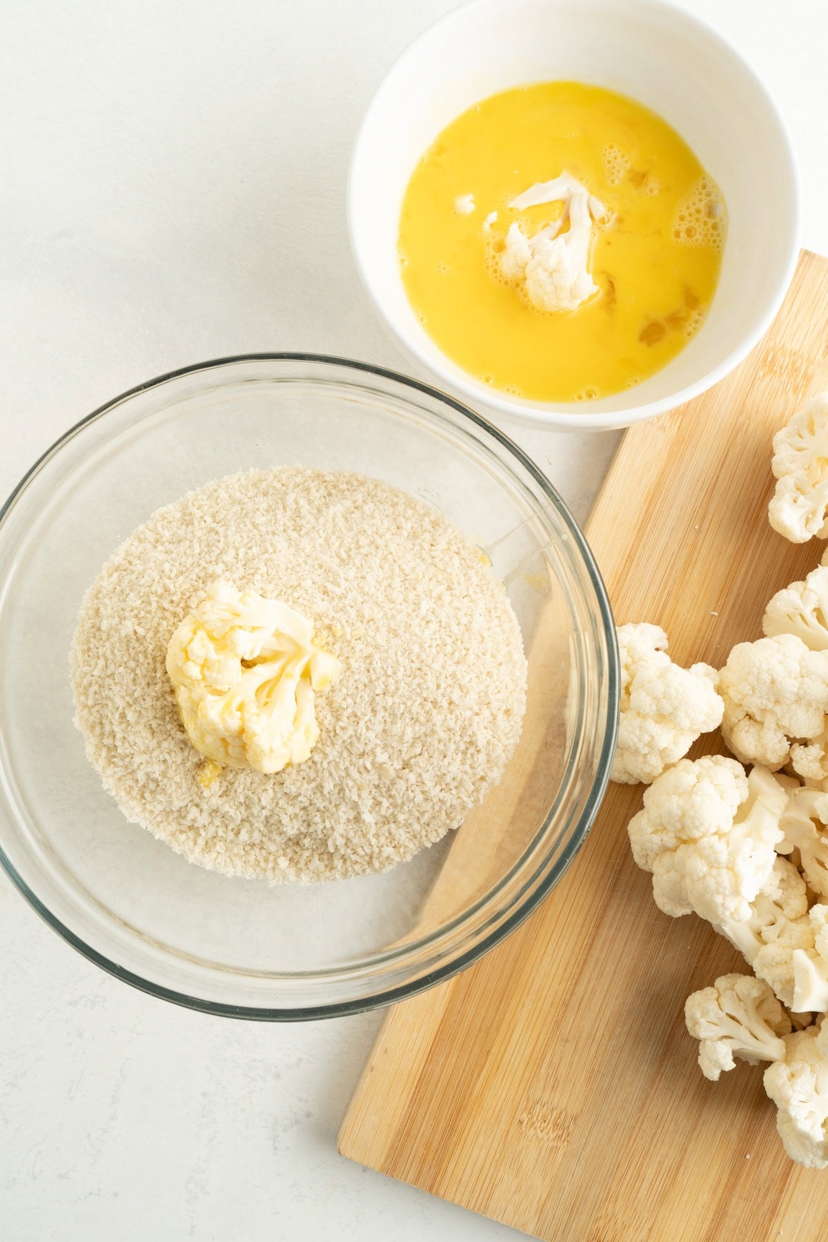 Cauliflower bites being coated in egg and dredged in panko bread crumbs.