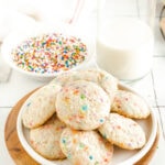 A plate of funfetti cake cookies beside a bowl of sprinkles and a glass of milk.