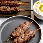 Close up of two kofta kebabs on a grey plate with some more in the background as well as dipping sauce