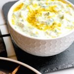 A white bowl on a grey slate plate filled with homemade Greek Tzatziki Sauce