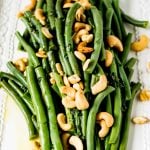 A white platter of green beans and cashews smothered in butter