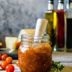 A jar of cherry tomato jam on a wood table with a small appetizer knife in the jar