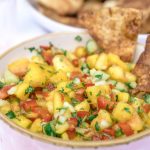 A salsa made with peaches and cucumbers in a pink bowl with cinnamon chips