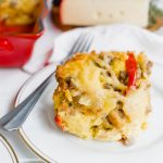 A large piece of a breakfast strata with sausage and red peppers on a plate with a fork.