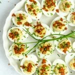 A round plate of devilled eggs topped with fresh chives and chorizo