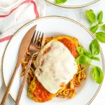 Baked chicken parmigiana on a white plate over pasta with fresh basil