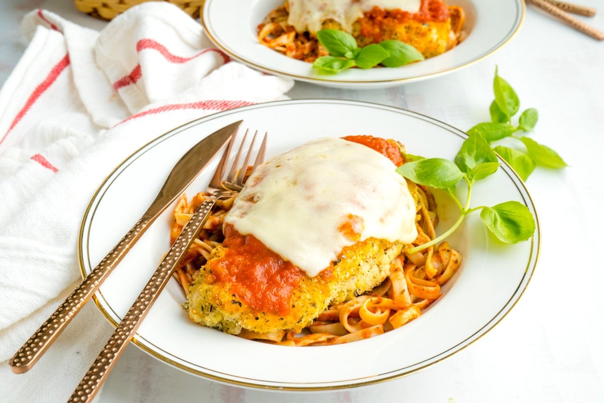 A plate of low carb chicken parmesan in a wide brimmed bowl with a fork and knife.