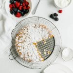 An overhead shot of an almond cake with two slices cut from it with berries and yogurt