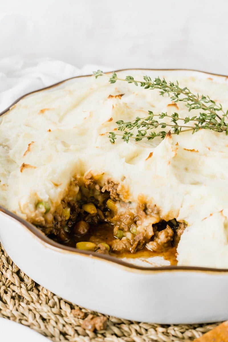 A cottage pie with a slice taken out topped with fresh thyme