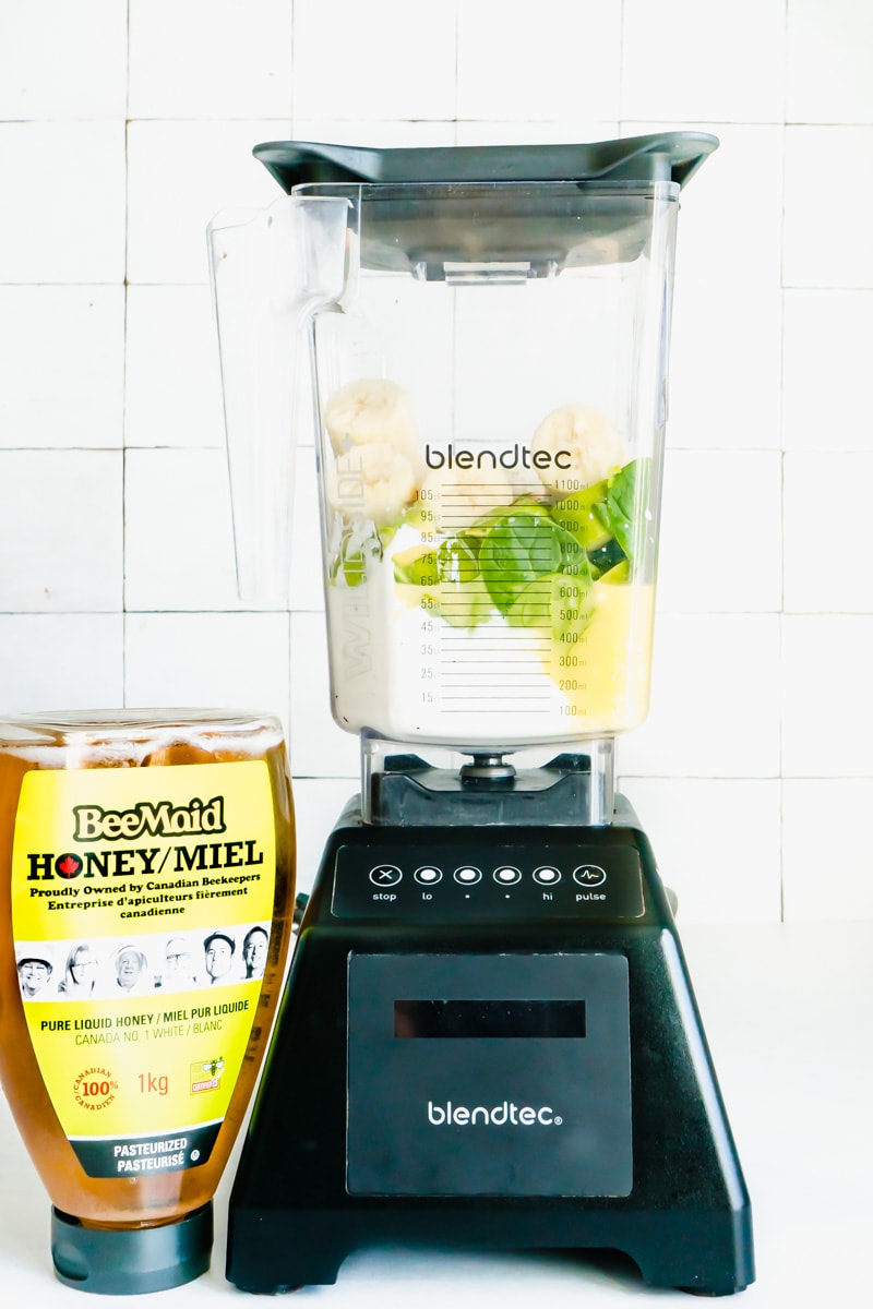 A blender with smoothie bowl ingredients beside a bottle of honey