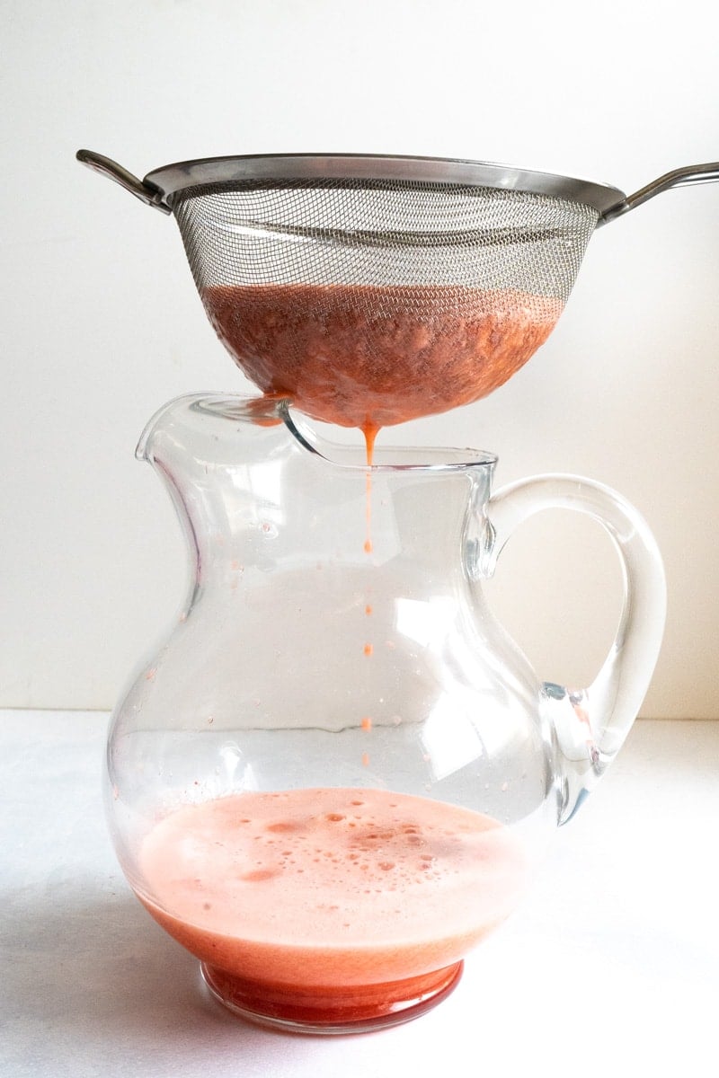 Strawberry juice being strained over a pitcher