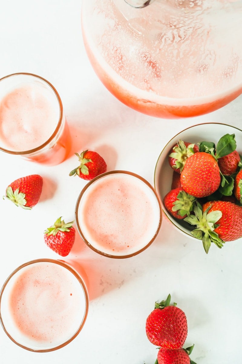 An overhead shot of 3 glasses of lemonade made with strawberries and a pitcher