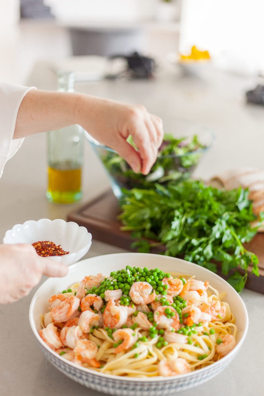 A bowl of shrimp and peas being sprinkled with hot pepper flakes.