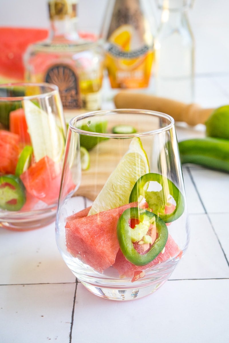 A glass filled with watermelon cubes, jalapeno slices and a lime wedge.